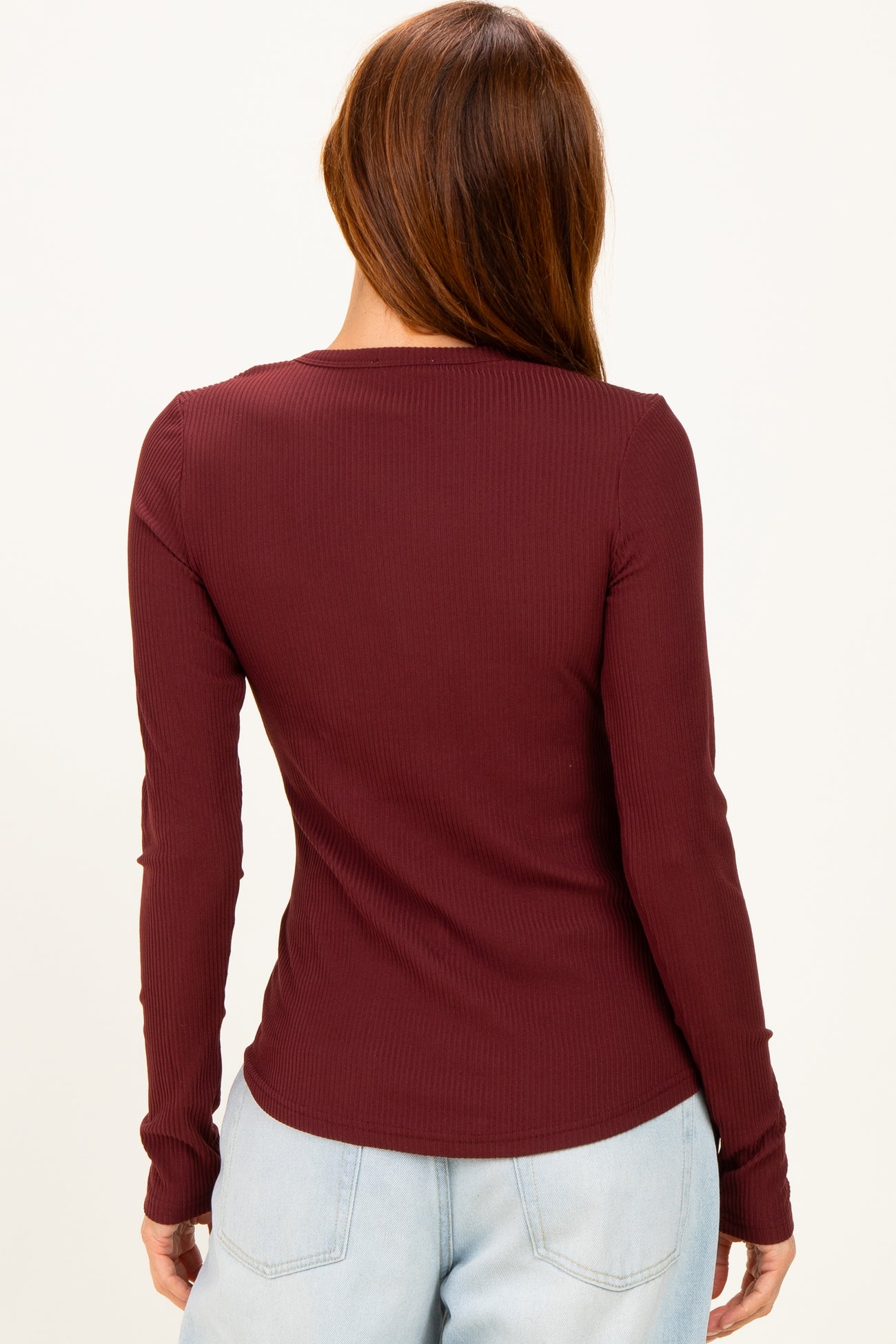 woman wearing a burgundy long sleeve ribbed top, view from the back, styled with light blue jeans
