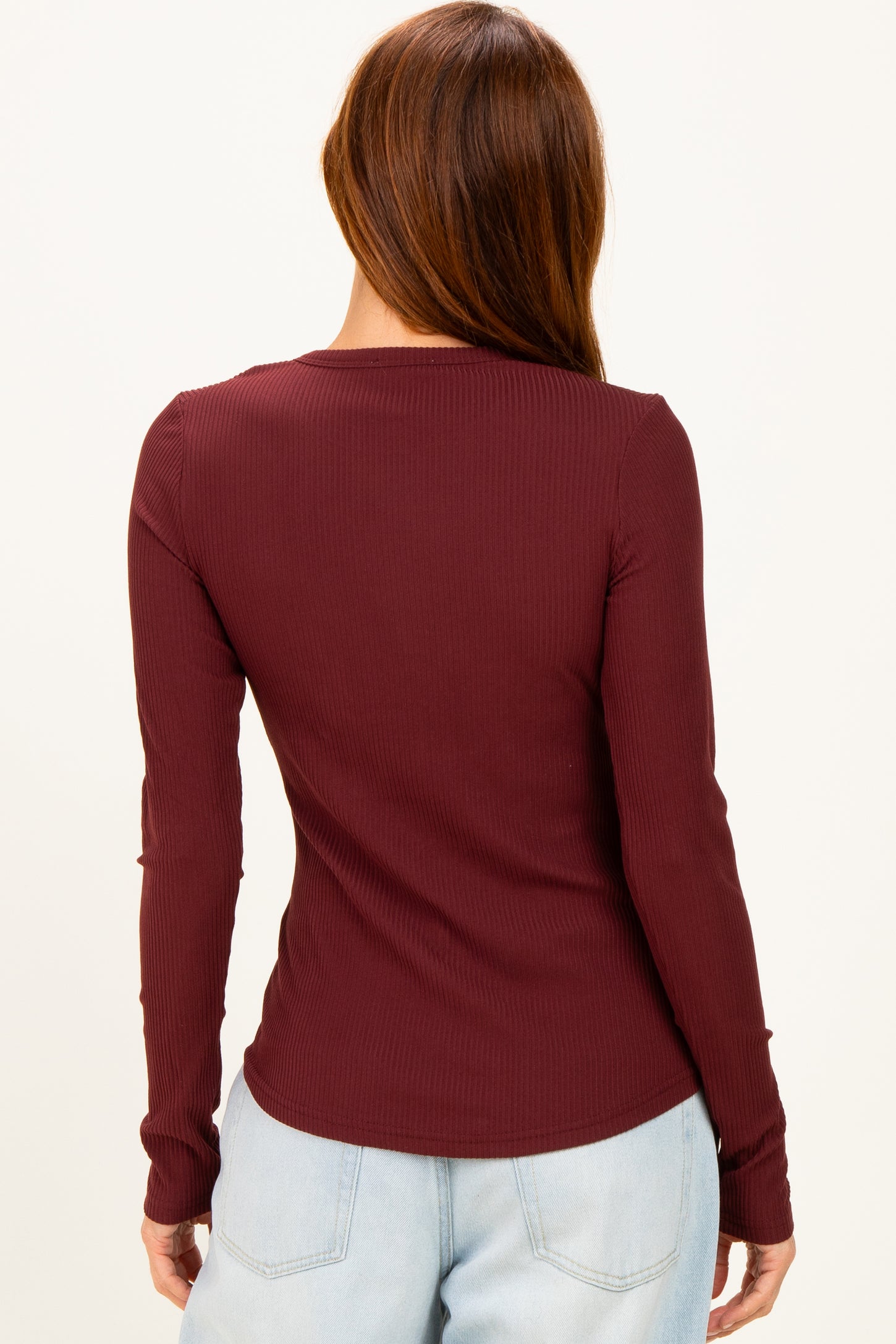 woman wearing a burgundy long sleeve ribbed top, view from the back, styled with light blue jeans