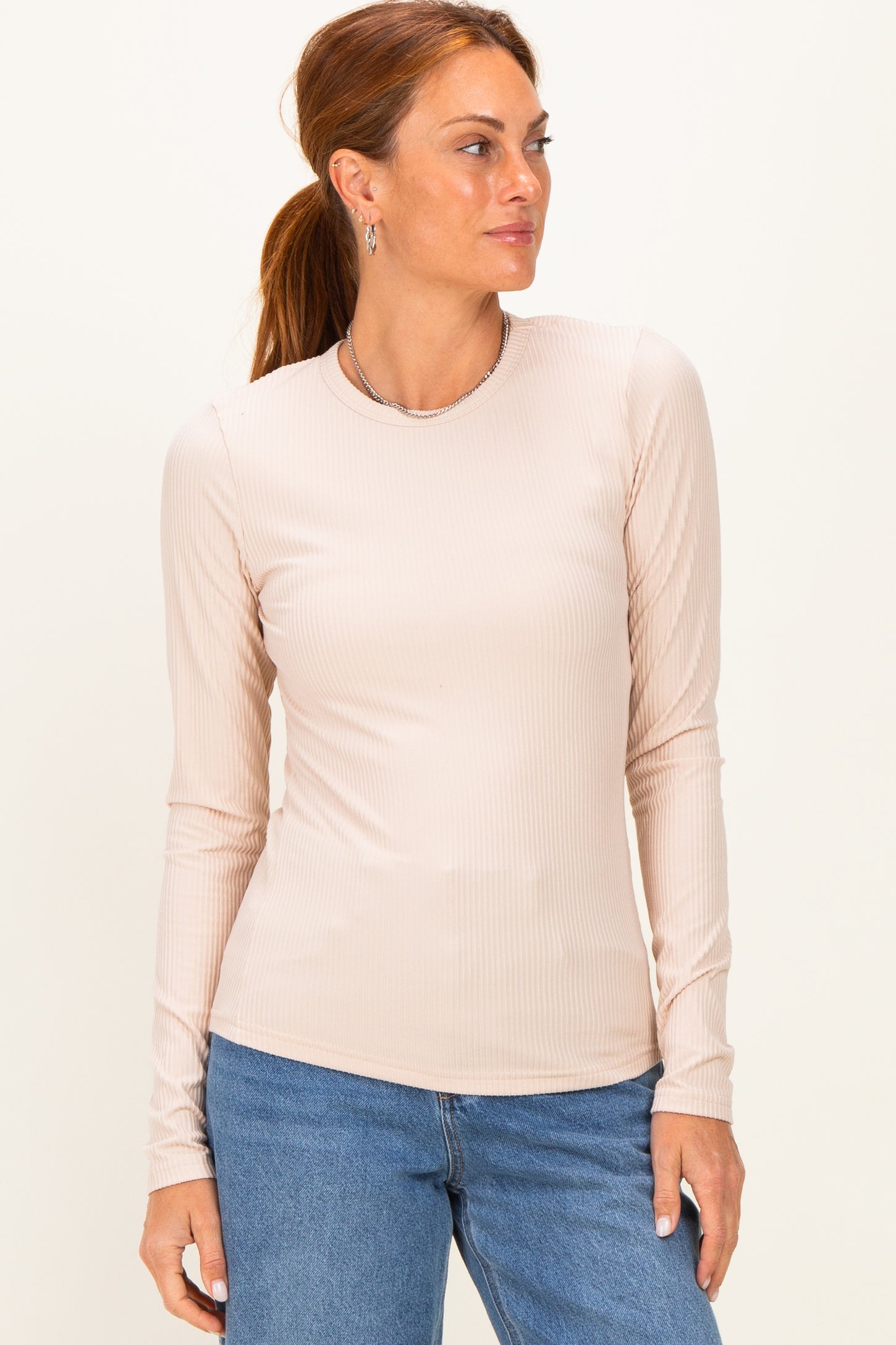 woman wearing a light beige long sleeve ribbed top with a round neckline and relaxed fit, paired with blue jeans