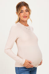 woman wearing a beige long sleeve maternity top and holding her baby bump