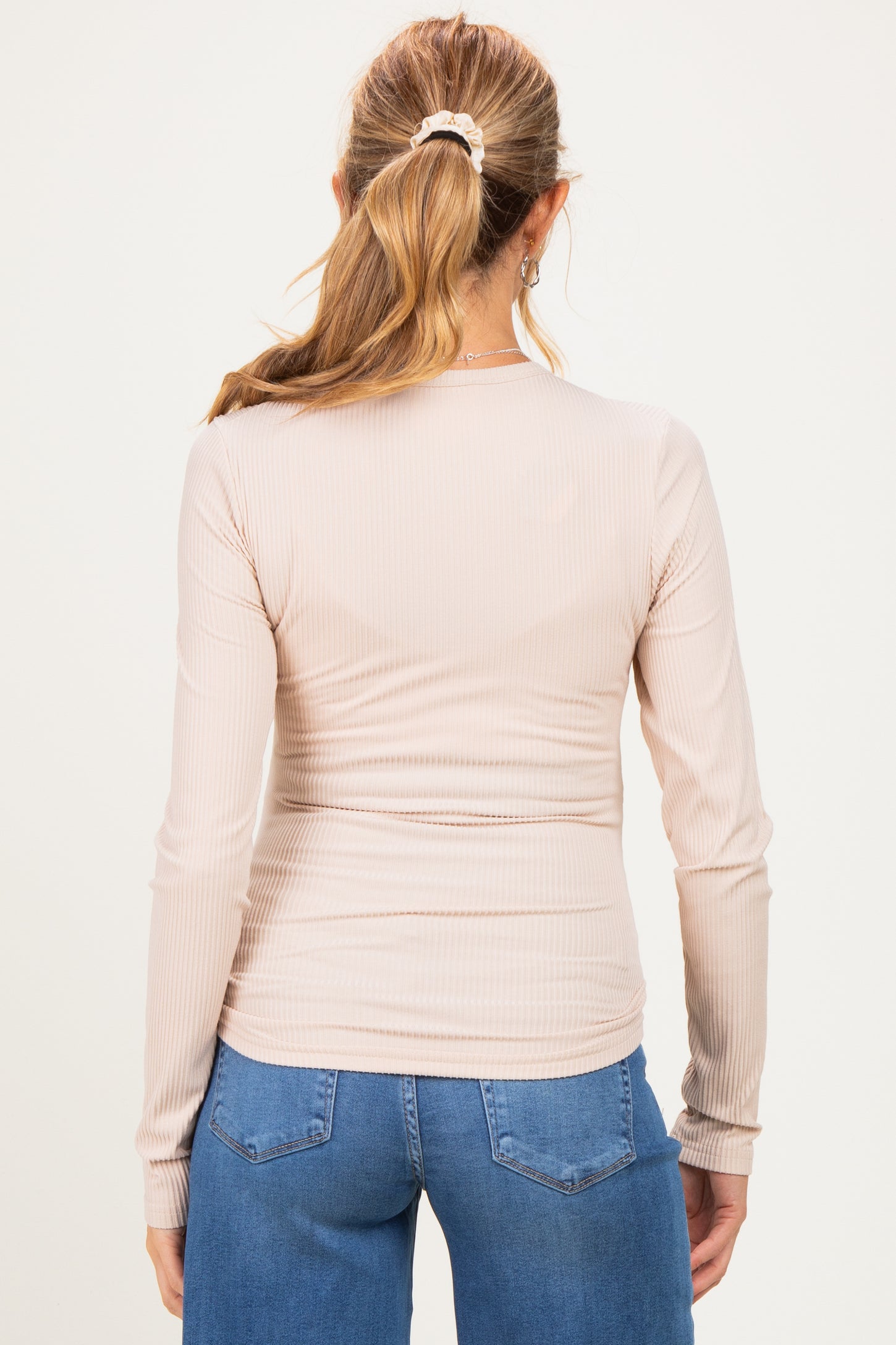 woman wearing a light beige long sleeve fitted maternity top, back view, paired with blue jeans