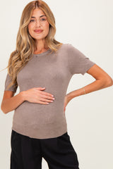 woman wearing a taupe short sleeve maternity top and holding her baby bump