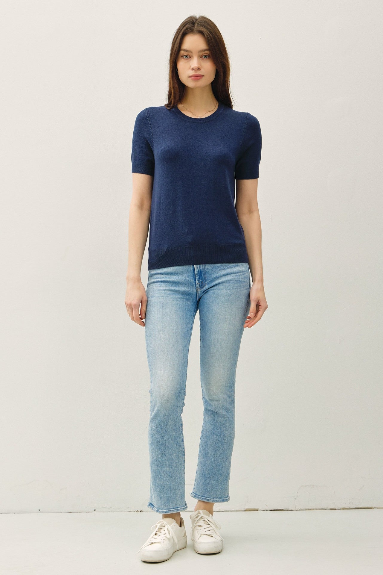 woman wearing a navy short sleeve knit top and light wash cropped jeans with white sneakers