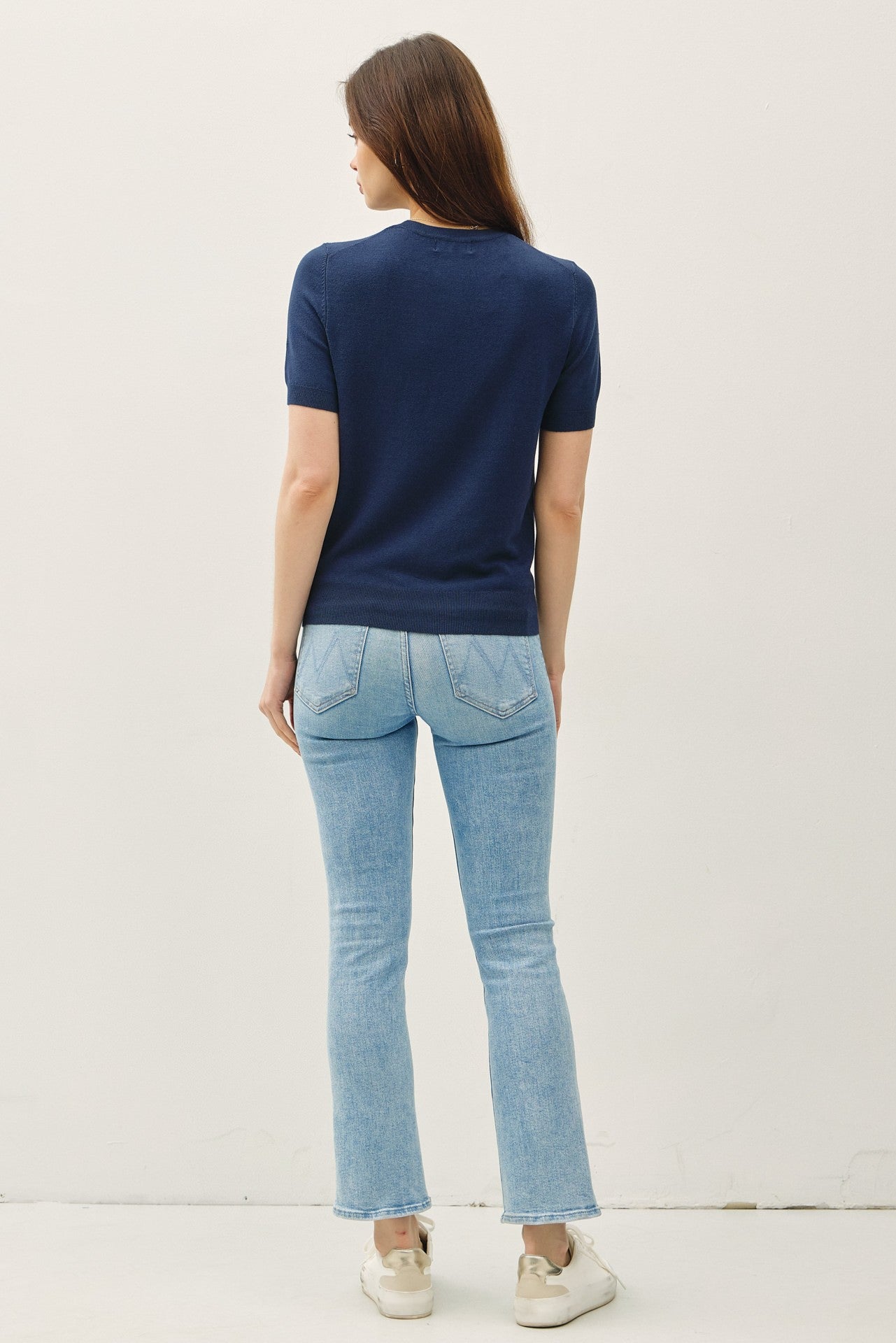 woman wearing a navy short sleeve top with light blue flared jeans and sneakers, viewed from the back