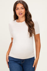 woman wearing a cream short sleeve maternity top and showing her baby bump with blue jeans