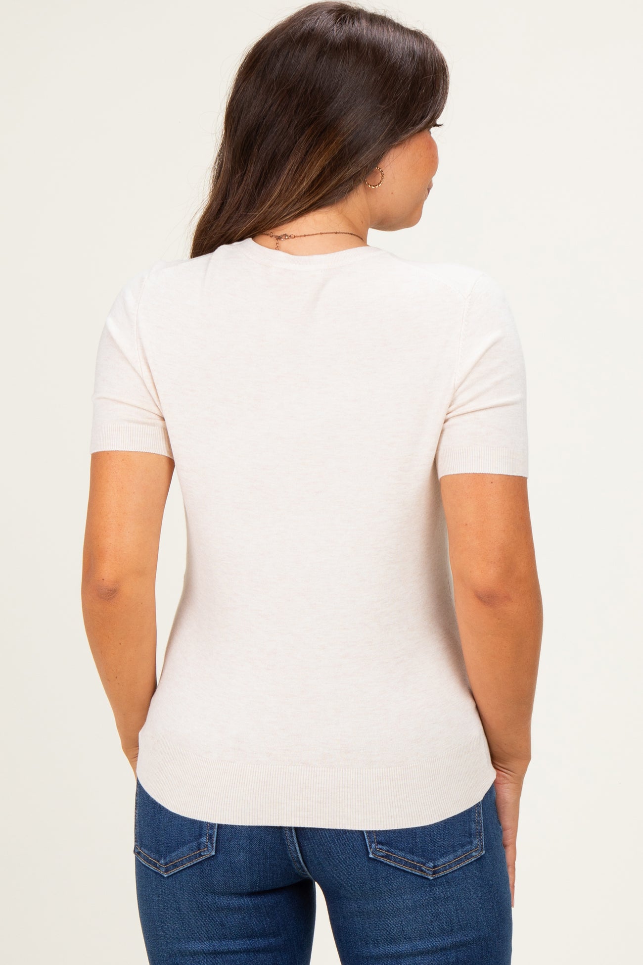 woman wearing a light beige short sleeve maternity top with a fitted silhouette, viewed from the back