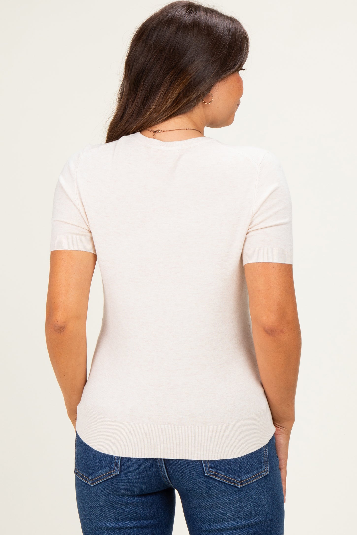 woman wearing a light beige short sleeve maternity top with a fitted silhouette, viewed from the back