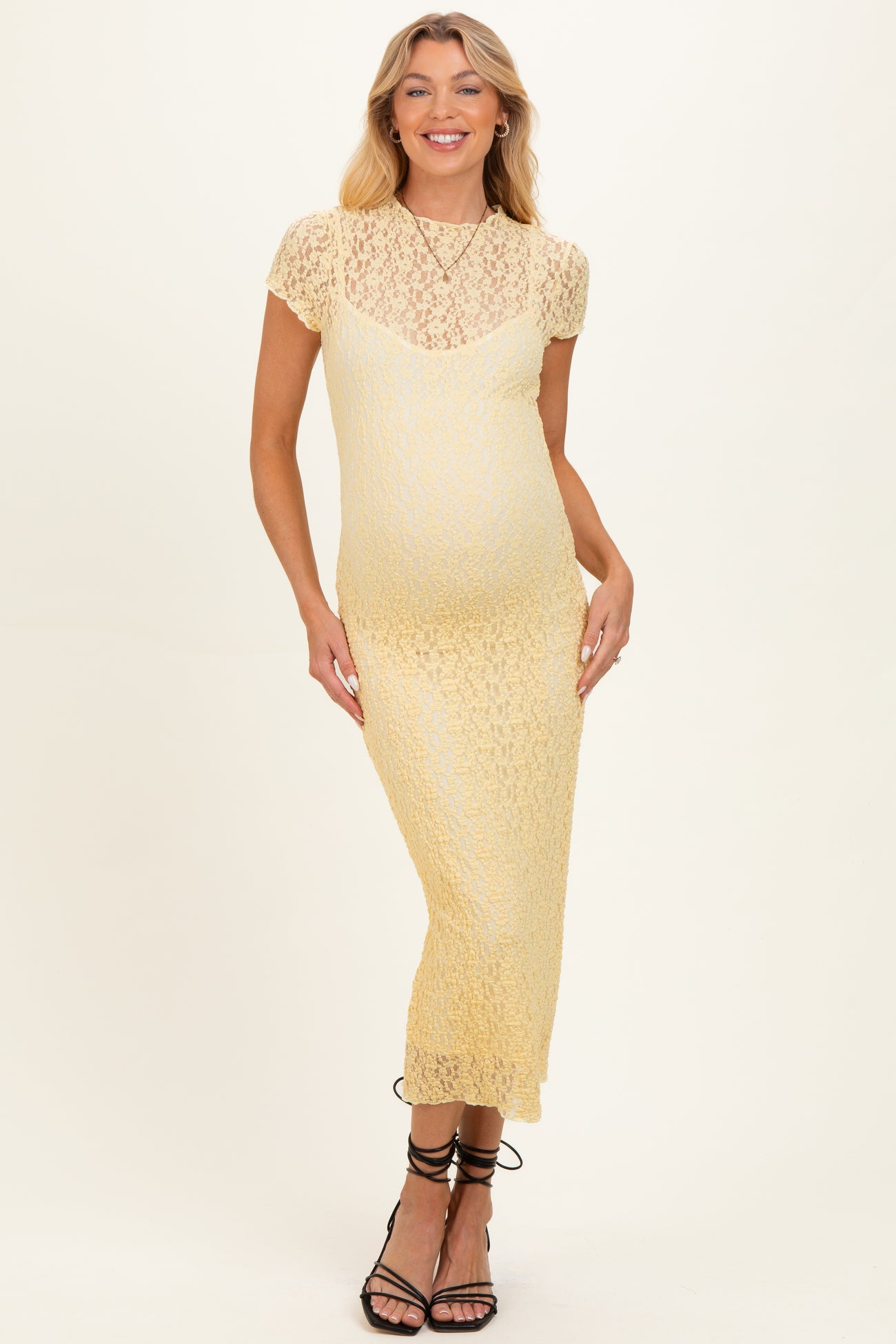 woman wearing a yellow lace maternity dress with short sleeves and a fitted silhouette, showcasing her baby bump