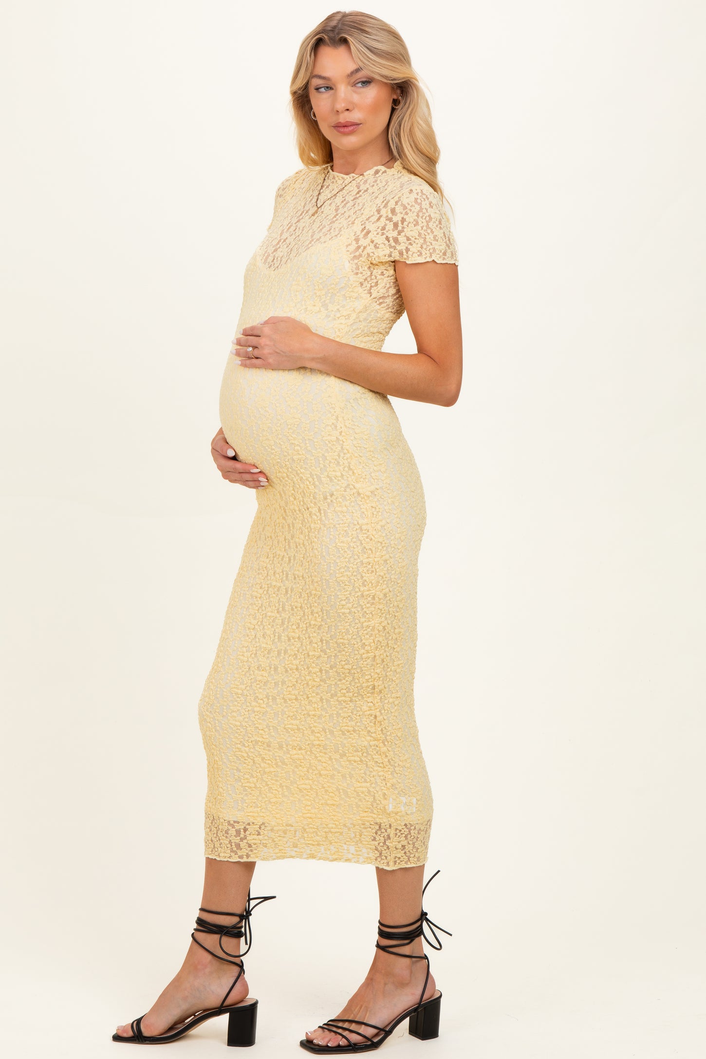 woman wearing a yellow lace maternity dress and holding her baby bump