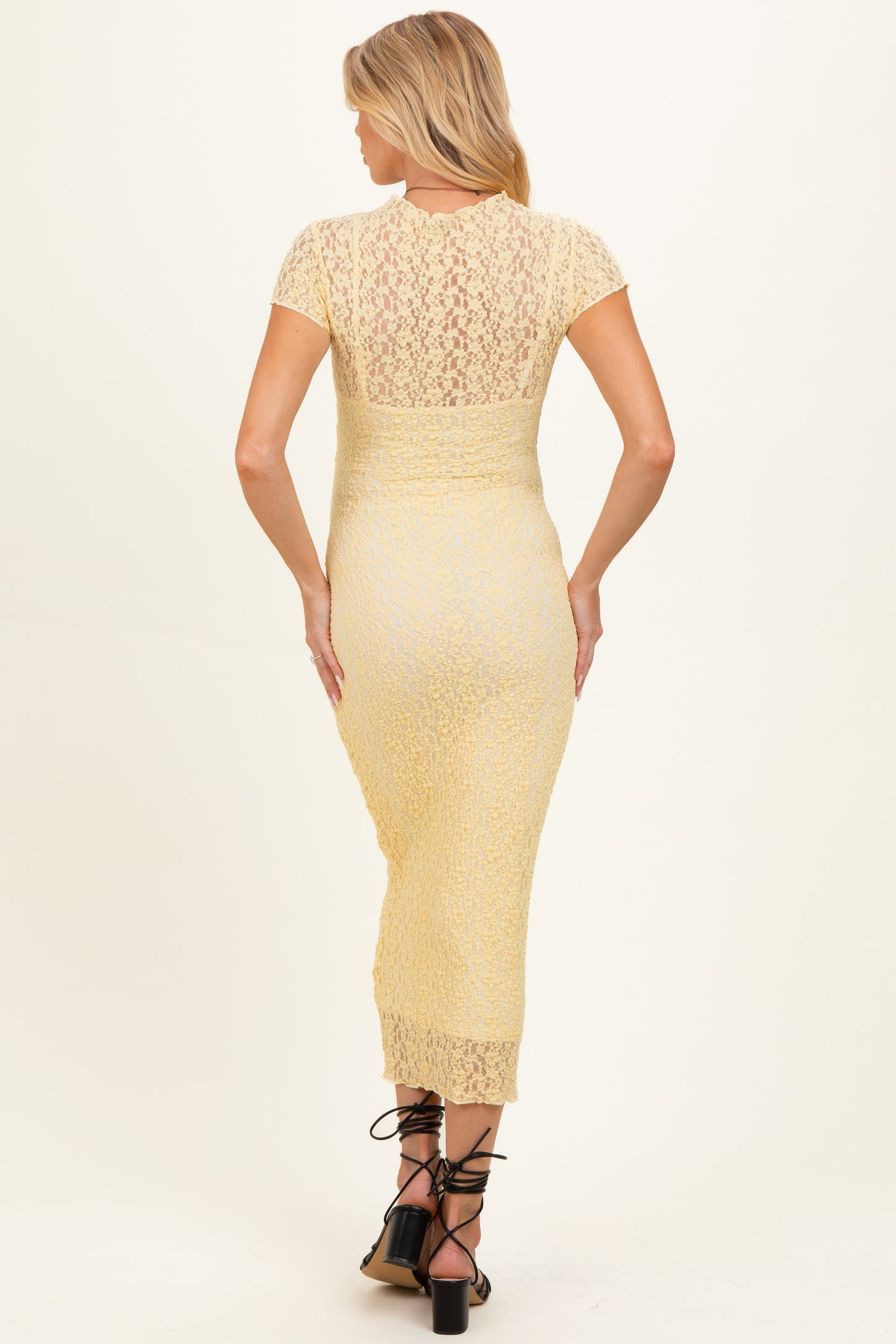woman wearing a yellow lace maternity dress with short sleeves and a fitted silhouette, showing a pregnant belly