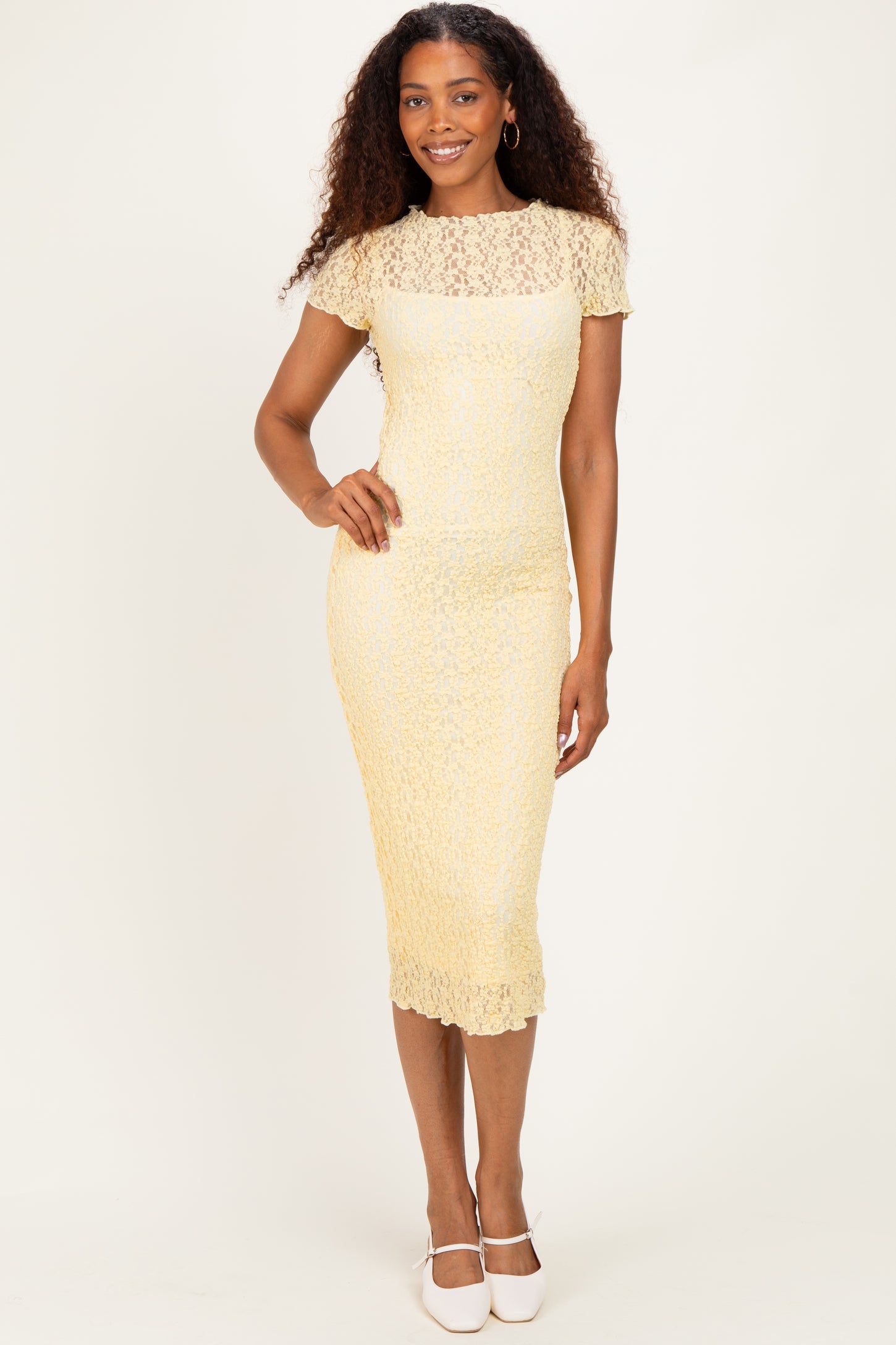 woman wearing a yellow lace midi dress with short sleeves, standing and smiling against a neutral background