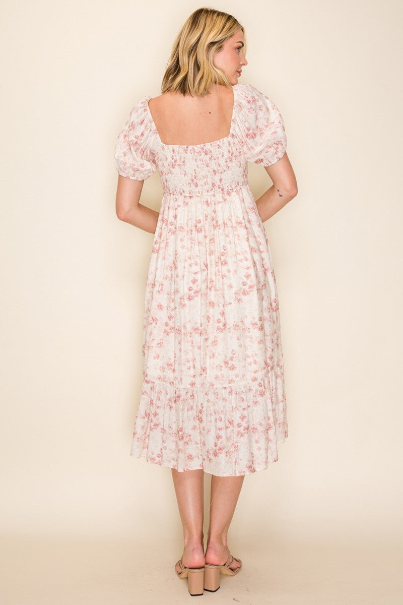 woman wearing a back view of a light pink floral midi dress with puff sleeves and a tiered skirt