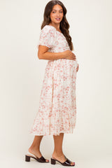 woman wearing a floral print maternity dress with a tiered hem and holding her baby bump