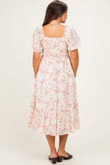 woman wearing a floral print maternity dress with puff sleeves and a tiered hem, showing off her baby bump