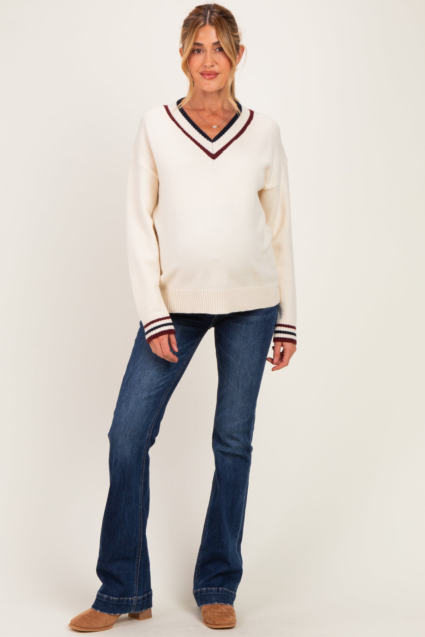 woman wearing a cream v-neck maternity sweater with burgundy and navy stripes, paired with blue flared jeans