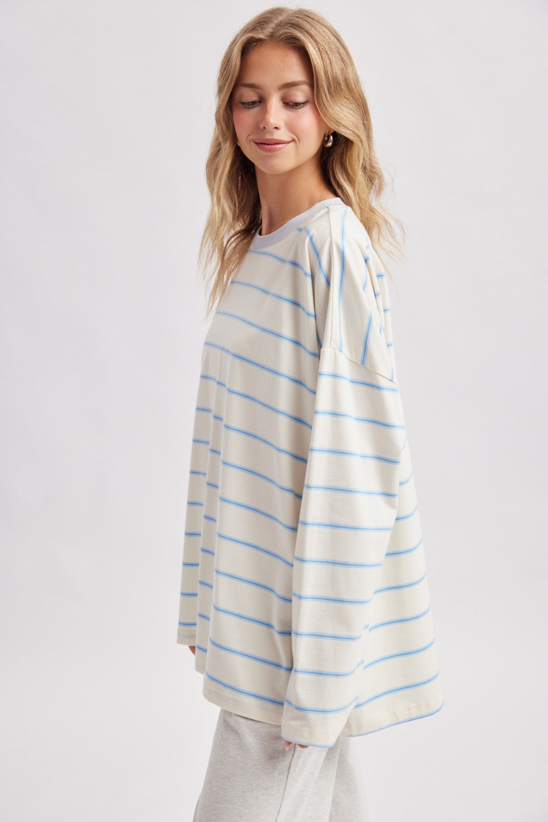 woman wearing a cream and light blue striped long sleeve oversized top with a relaxed fit and round neckline