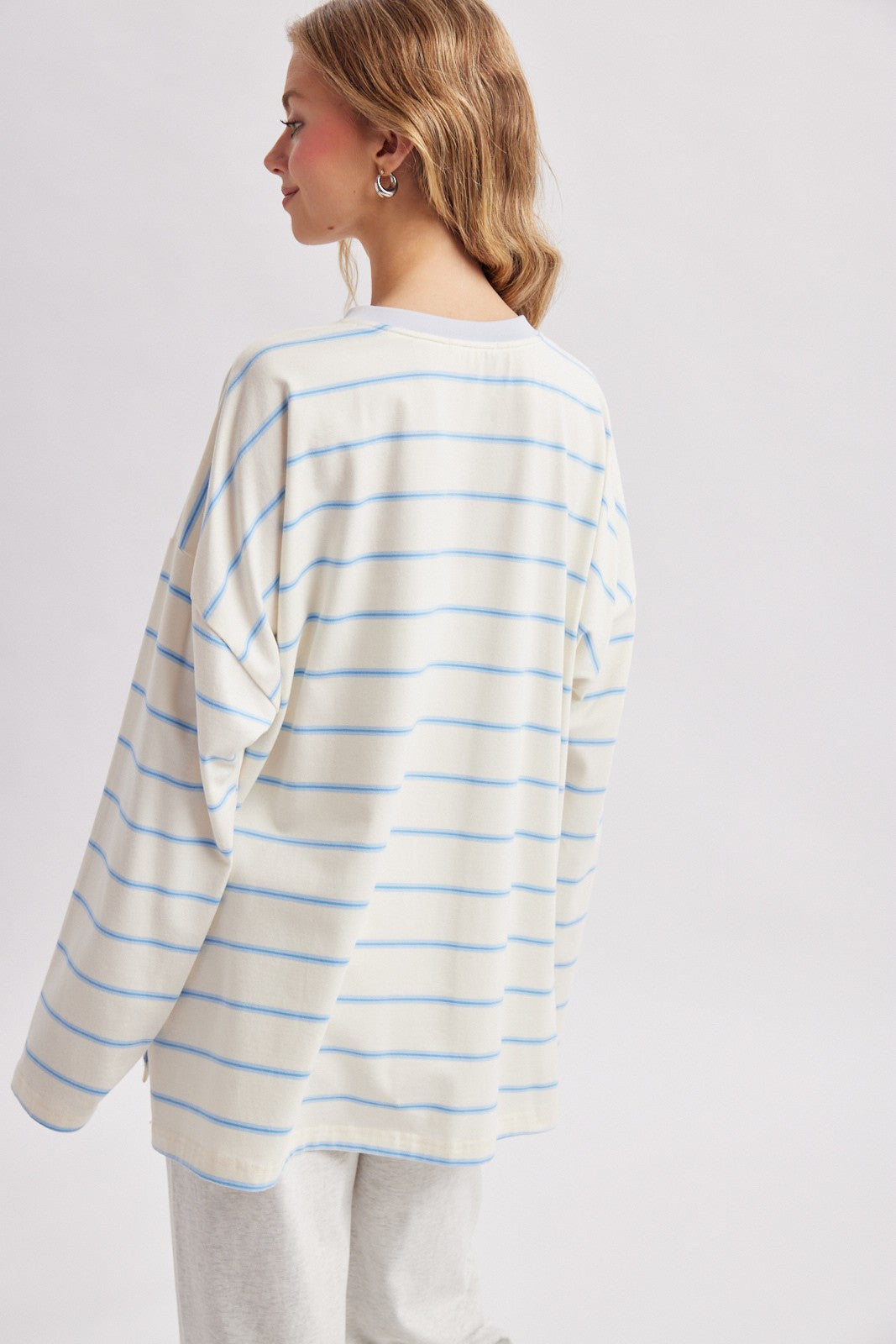 woman wearing a white oversized long sleeve top with blue stripes, seen from the back