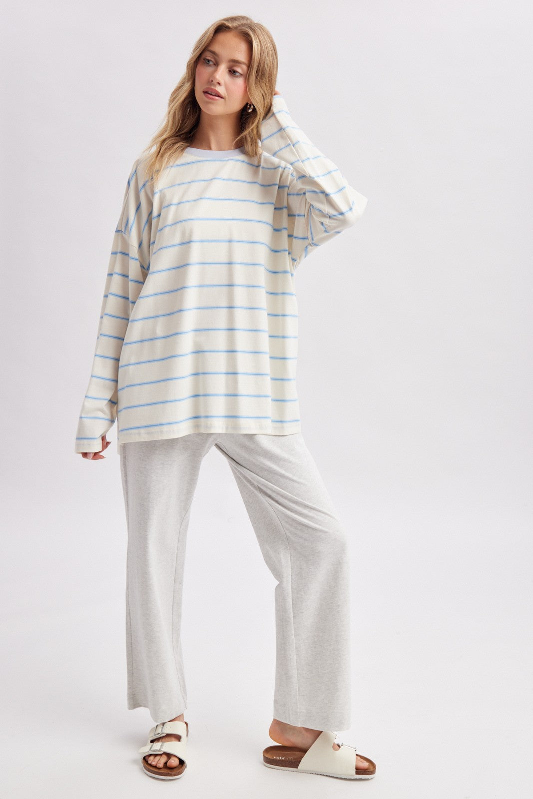 woman wearing a cream and blue striped oversized long sleeve top with gray wide-leg pants and white sandals