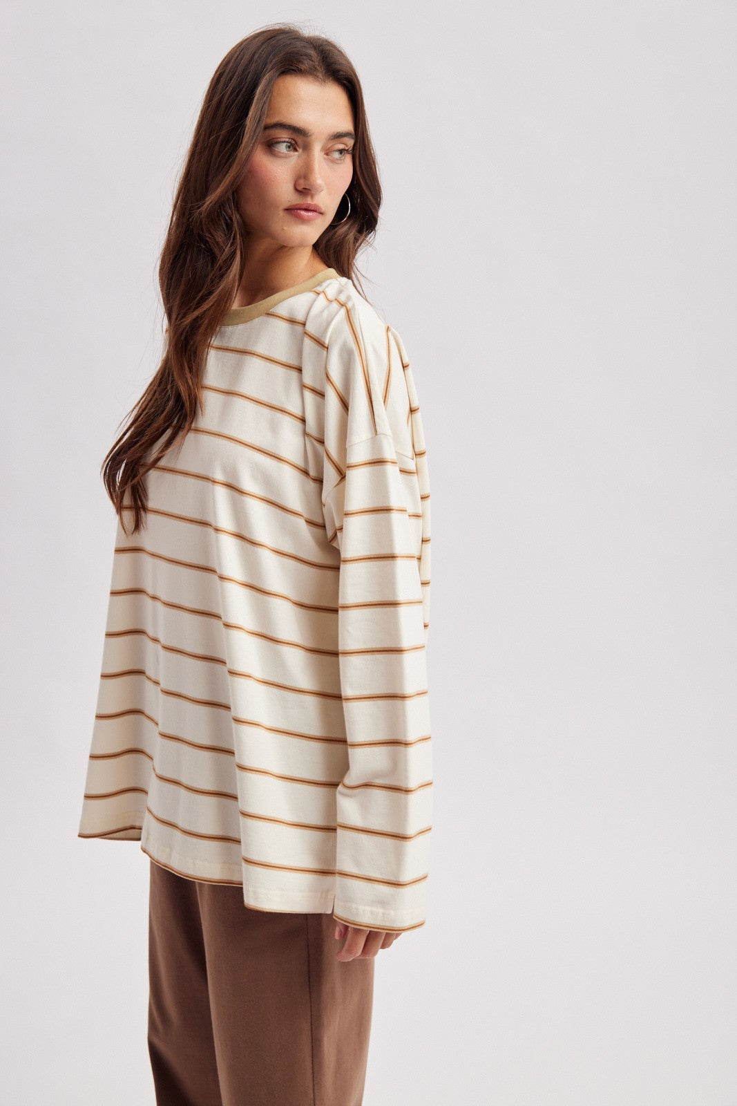 woman wearing a cream long sleeve striped top with brown stripes and relaxed fit, styled with brown trousers
