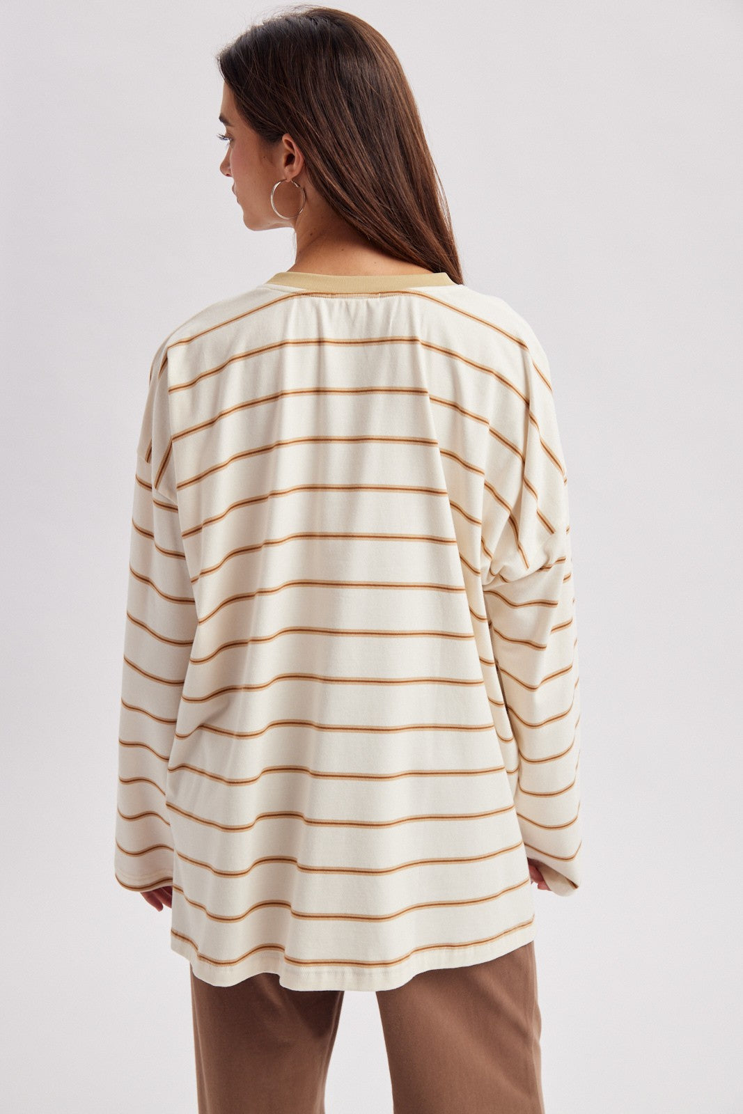 woman wearing a cream and mustard striped oversized long sleeve top, seen from the back