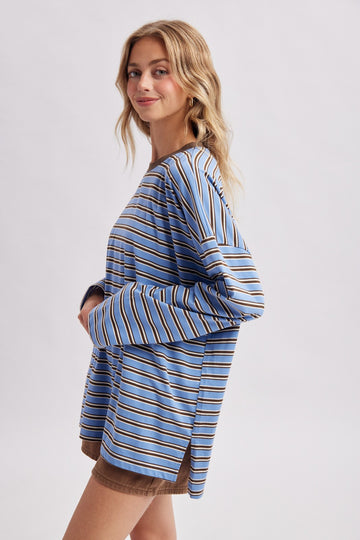woman wearing a blue striped long sleeve top with wide sleeves and side slits, paired with brown shorts