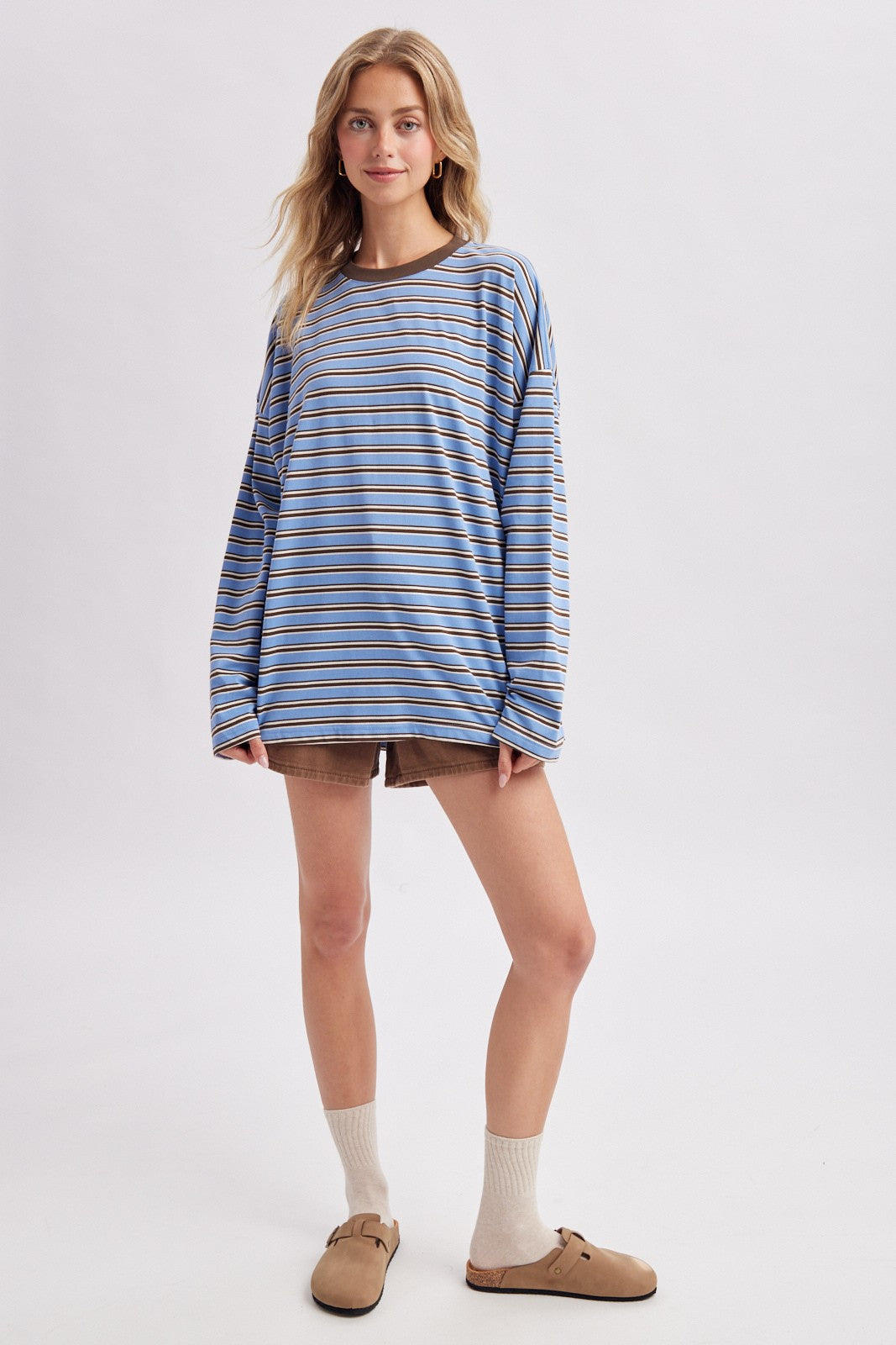 woman wearing a blue and brown striped long sleeve oversized shirt with brown shorts and cream-colored socks