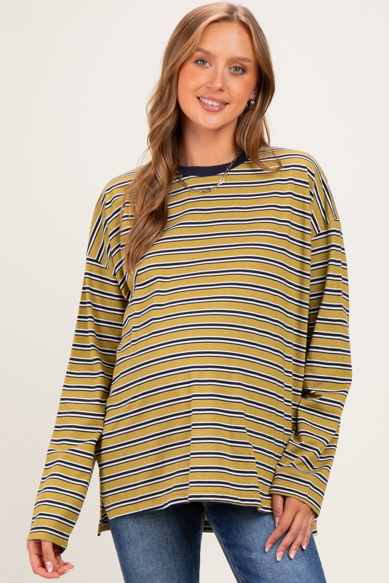 woman wearing a mustard striped maternity top with long sleeves, smiling and showing her baby bump
