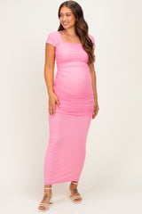woman wearing a pink maternity maxi dress with short sleeves and ruching, showcasing her baby bump