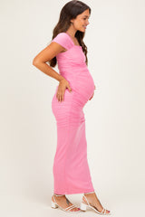 woman wearing a pink maternity maxi dress with ruching and holding her baby bump