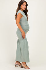 woman wearing a sage green maternity dress with a fitted bodice and flared bottom, showing her baby bump