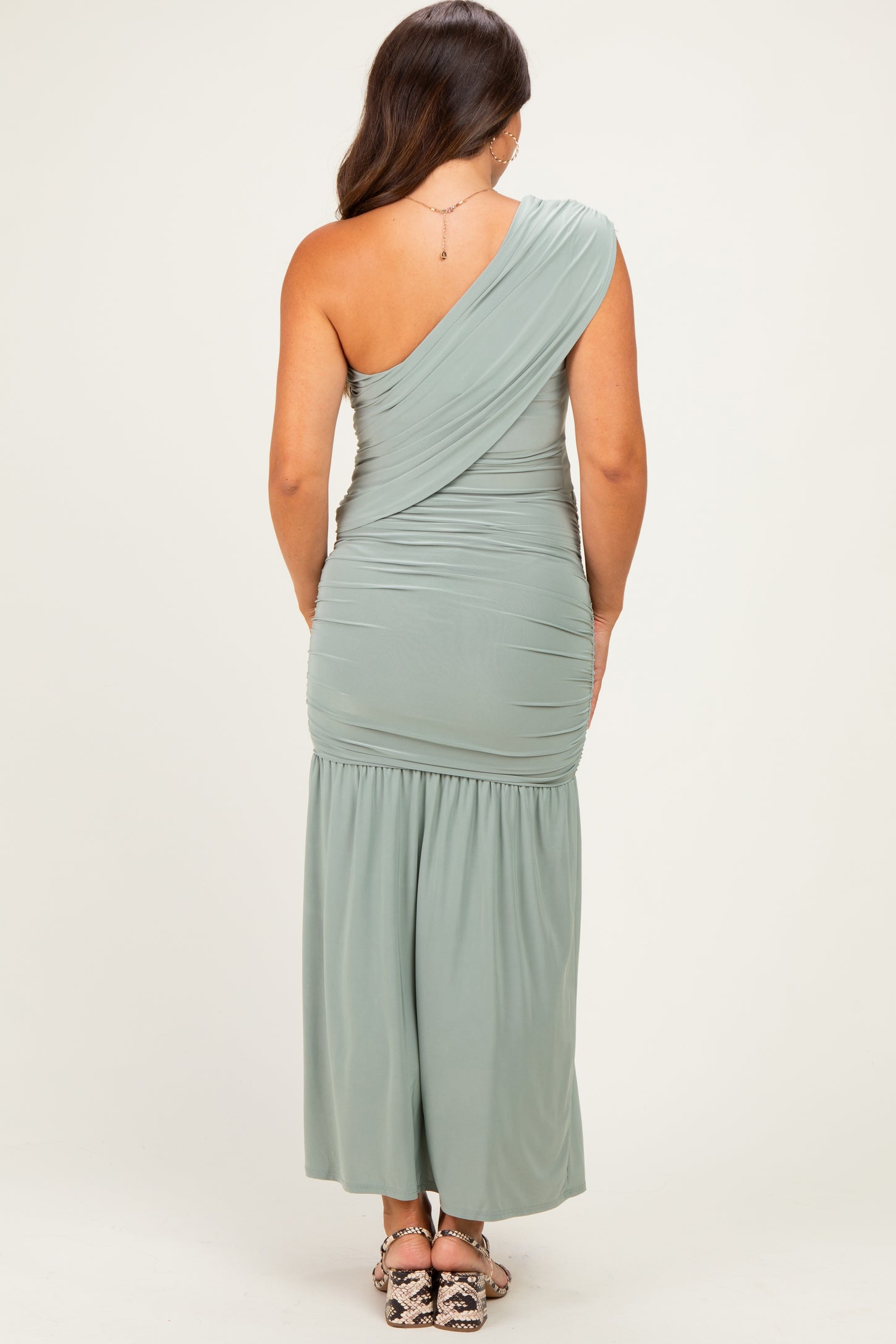 woman wearing a sage green one shoulder maternity dress with ruched detailing and a flowy bottom