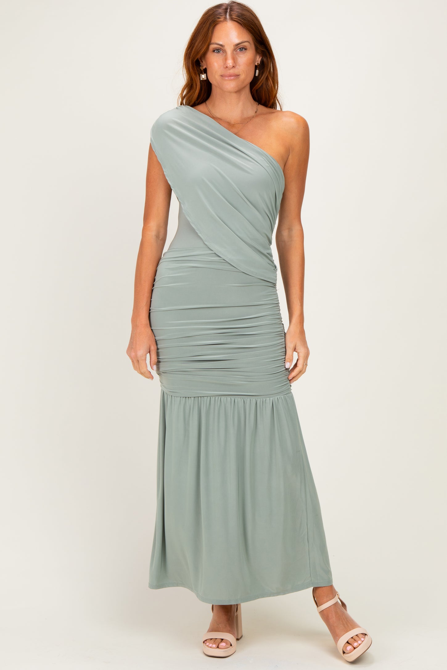 woman wearing a sage green one-shoulder maxi dress with ruching and a flowy bottom