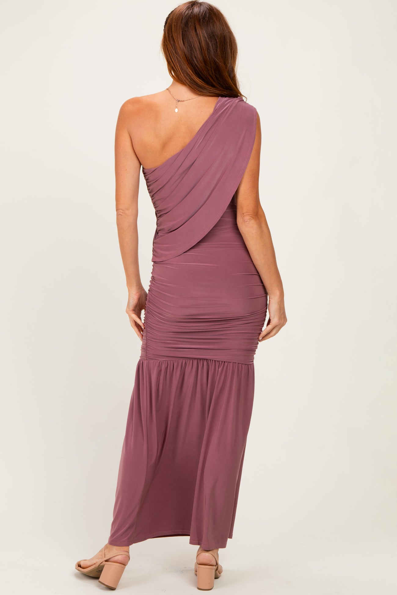 woman wearing a mauve one-shoulder maxi dress with gathered detailing and a flowing skirt, view from the back