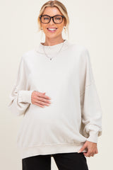 woman wearing a light beige oversized maternity sweatshirt and holding her baby bump