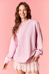 woman wearing a pink oversized sweatshirt with a relaxed fit and a ribbed collar, styled with a ruffled pink mini skirt