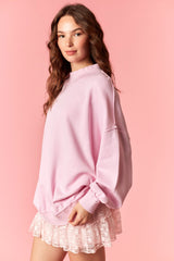 woman wearing a oversized pink sweatshirt paired with a pink ruffled skirt against a pink background