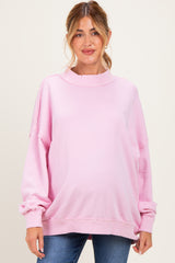 woman wearing a pink oversized maternity sweatshirt with distressed details and a visible baby bump