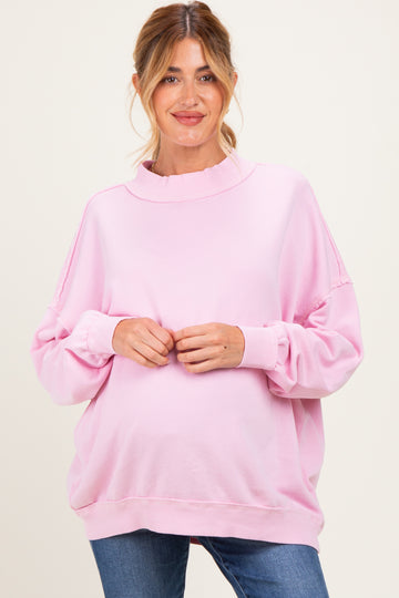 woman wearing a light pink oversized maternity sweat shirt with a ruffled neck and a visible baby bump
