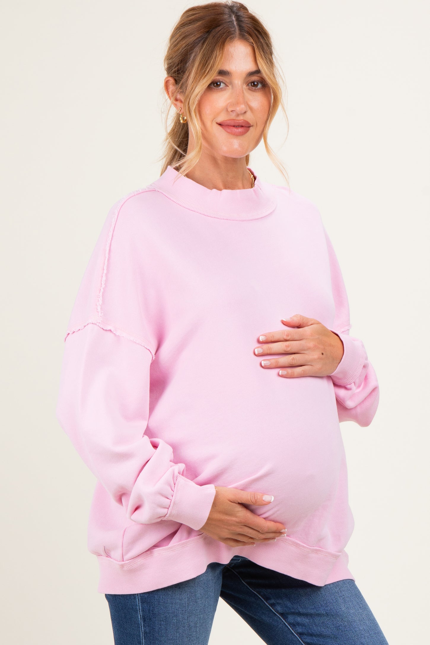 woman wearing a light pink maternity sweatshirt and holding her baby bump