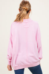 woman wearing a light pink oversized maternity sweatshirt with a back design detail and long sleeves