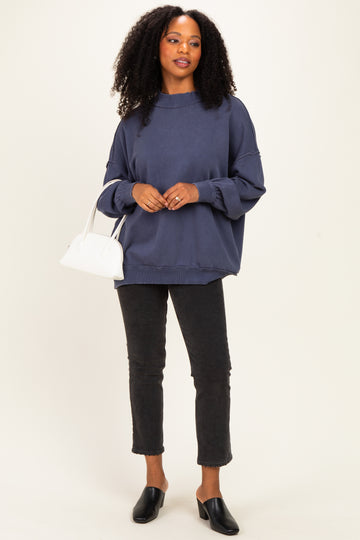 woman wearing a navy oversized sweatshirt with balloon sleeves and black cropped jeans, holding a white handbag
