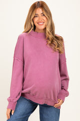 woman wearing a purple oversized maternity sweatshirt and smiling, with a visible baby bump