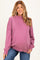 woman wearing a purple oversized maternity sweatshirt and smiling, with a visible baby bump