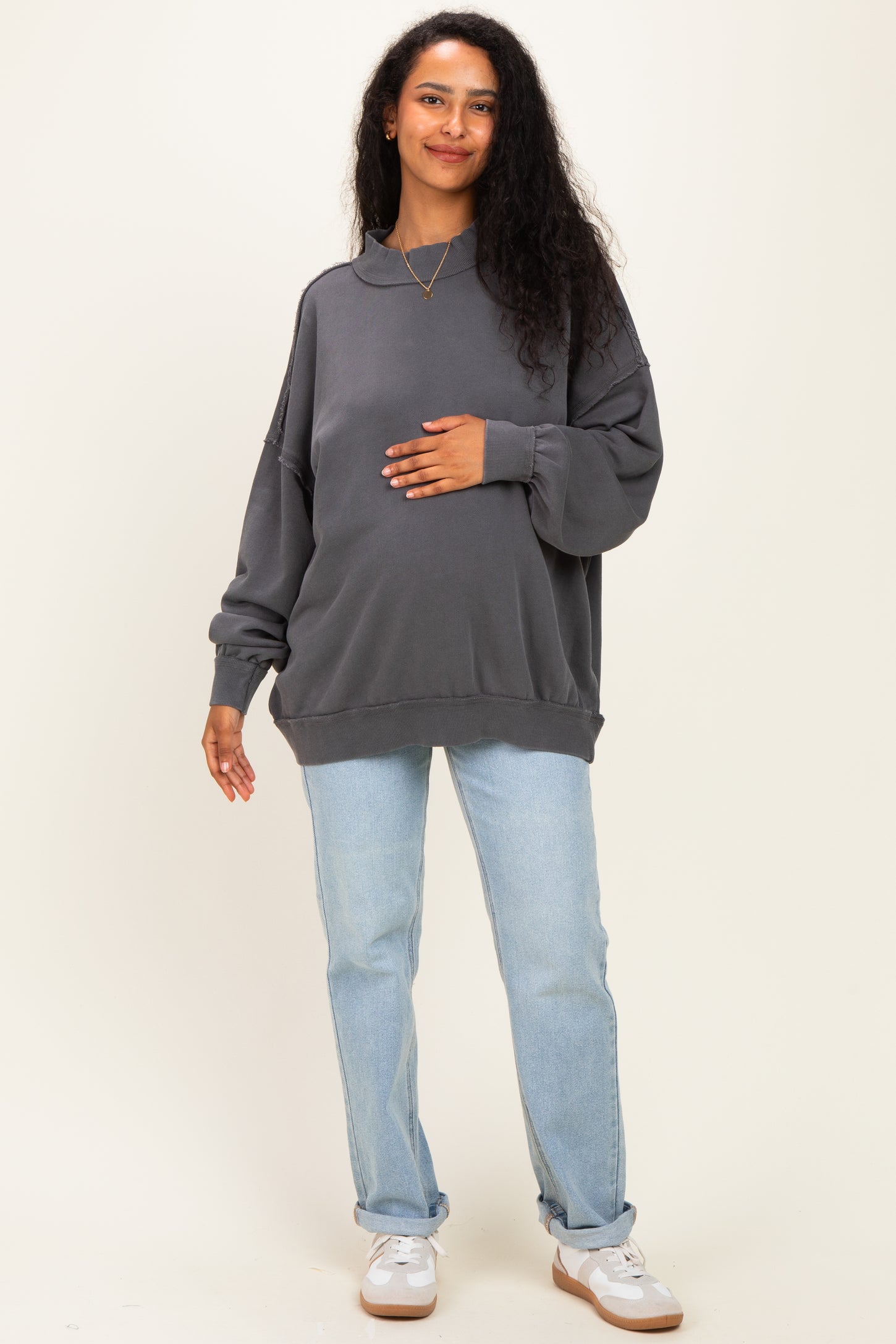 woman wearing a charcoal gray oversized maternity sweatshirt and blue jeans, holding her baby bump