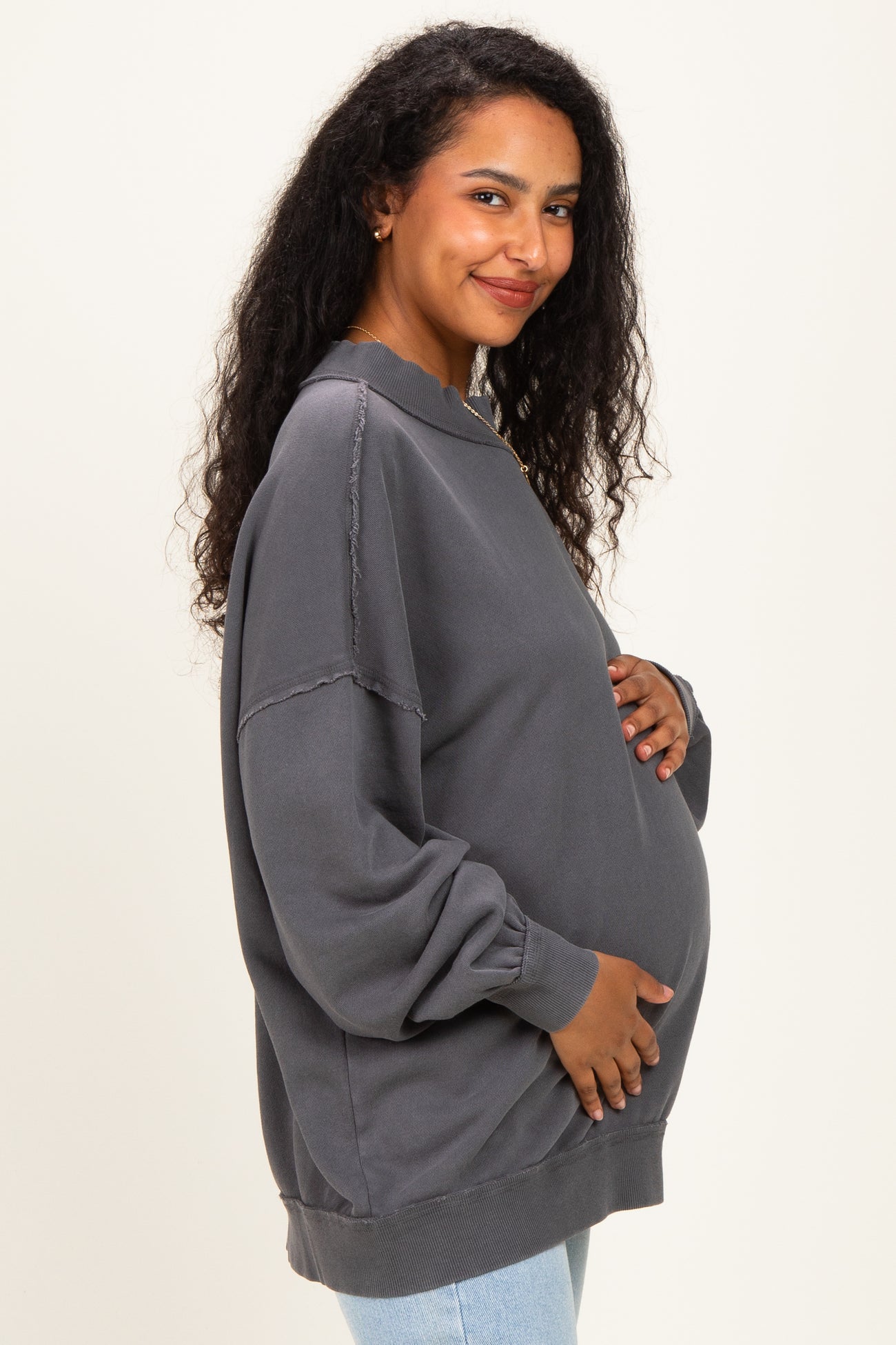 woman wearing a gray oversized maternity sweatshirt and holding her baby bump