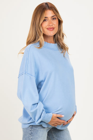 woman wearing a light blue oversized maternity sweatshirt and gently cradling her baby bump