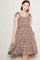 woman wearing a brown floral sundress with tie straps and a flared skirt, standing with one hand in her pocket