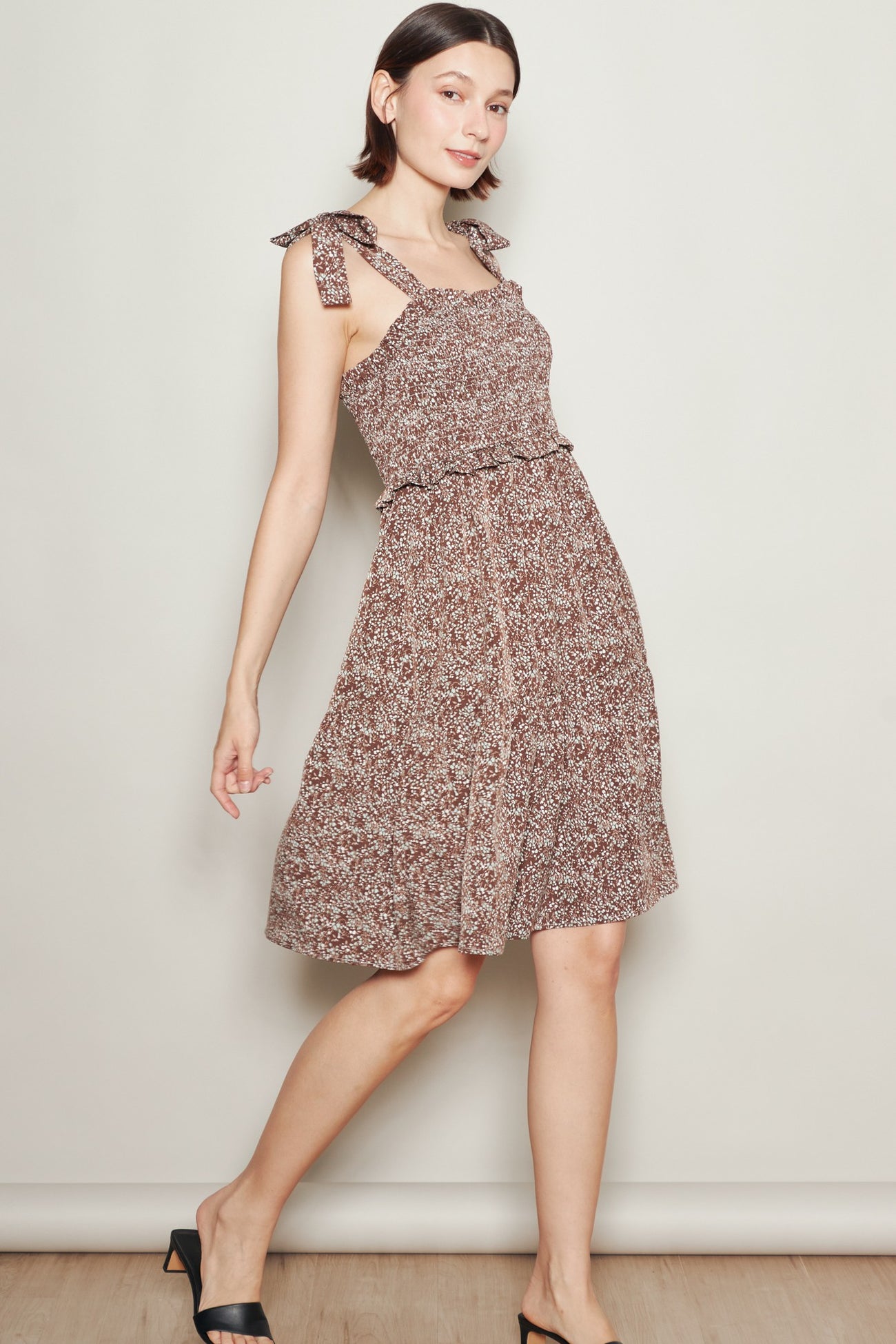 woman wearing a brown floral midi dress with tie straps and a fitted waist, posed against a neutral background