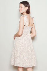 woman wearing a light pink floral midi dress with shoulder ties and a fitted bodice