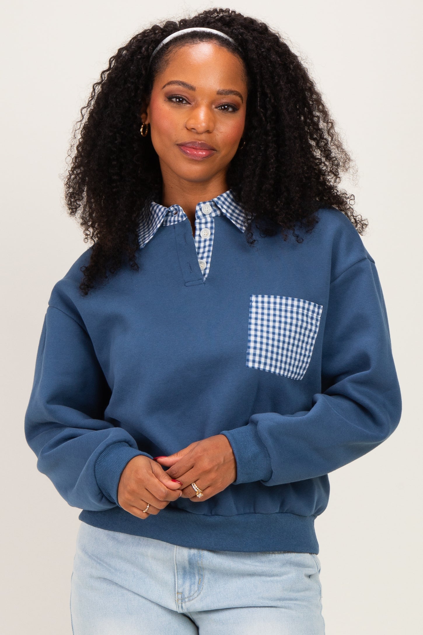 woman wearing a dark blue sweatshirt with a gingham collar and pocket, styled with light denim jeans